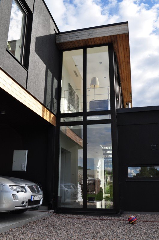 Nowoczesny dom z czarną elewacją i wysokimi oknami, widoczny samochód i piłka na żwirowym podłożu.