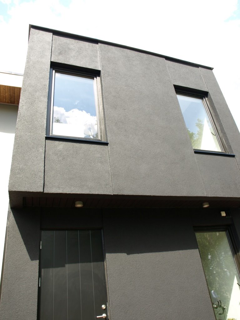 Elewacja nowoczesnego domu w odcieniach szarości z dwoma oknami o czarnych ramach i ciemnymi drzwiami wejściowymi.