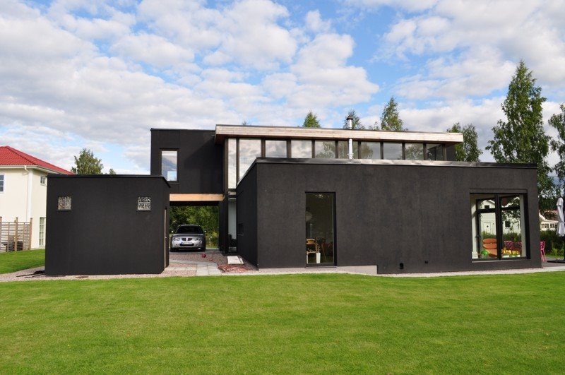 Czarny, nowoczesny dom z dużymi oknami, garażem podłączonym do domu, widok z zewnątrz na zadbany trawnik i błękitne niebo z chmurami.