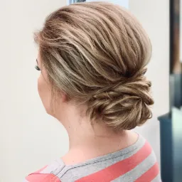 Upięcie włosów blond, kok niski z tyłu głowy, widok z boku na kark i fragment ramienia w bluzce w szaro-różowe paski.