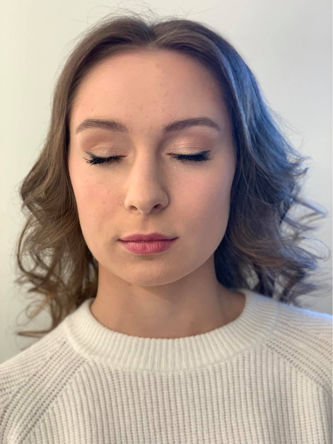 Portret kobiety z zamkniętymi oczami, prezentujący delikatny makijaż ślubny z eyelinerem w stylu cat-eye i różowymi ustami, włosy ułożone w luźne fale.