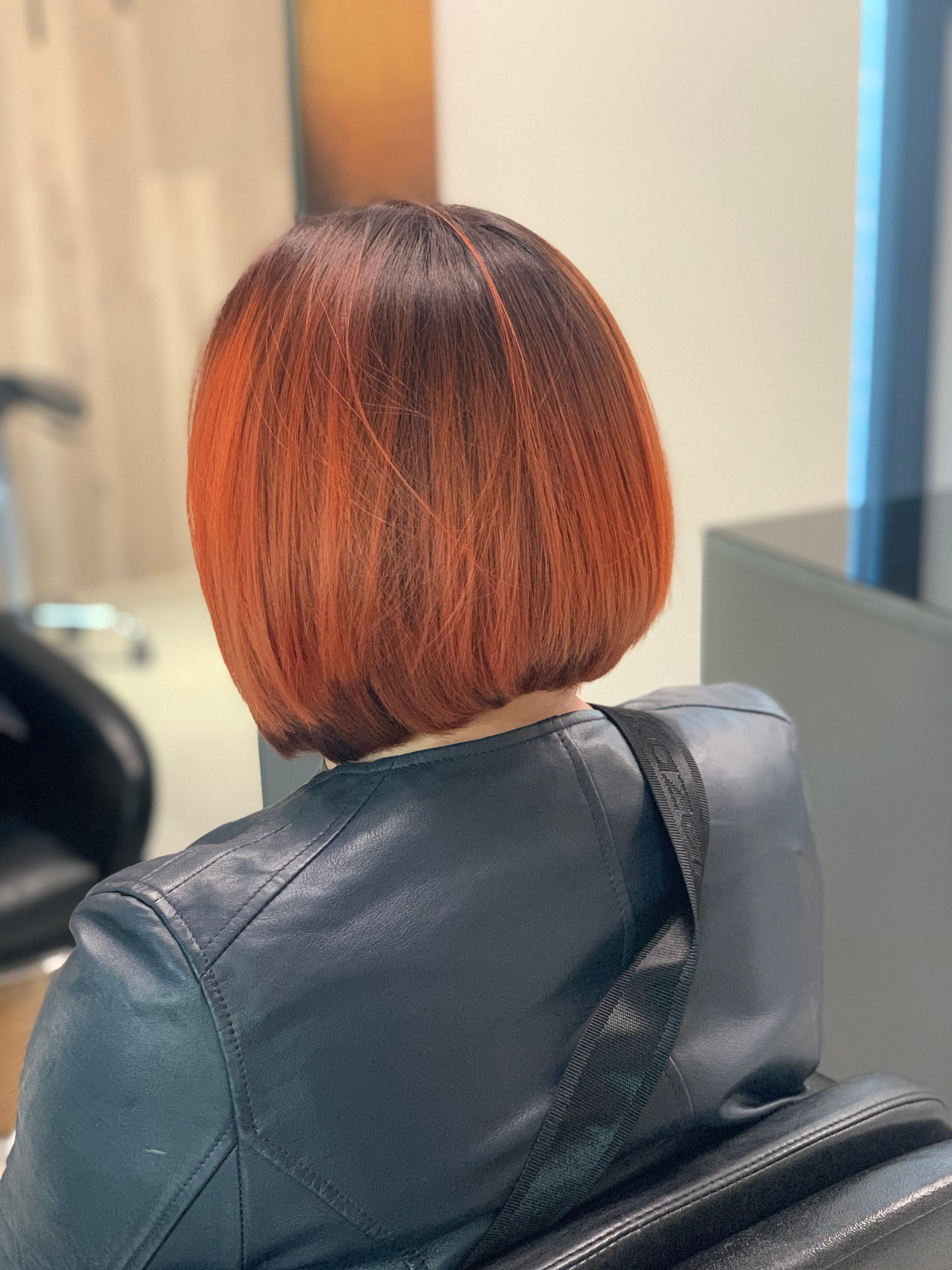 Krótkie, proste włosy w odcieniach brązu i miedzi, widok z tyłu, klientka w czarnej skórzanej kurtce siedzi na fotelu.