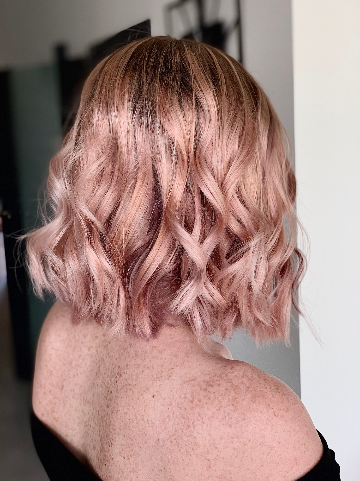 Krótkie, falowane włosy w odcieniach różowego blondu, widok z tyłu, odsłonięte ramię z piegami.