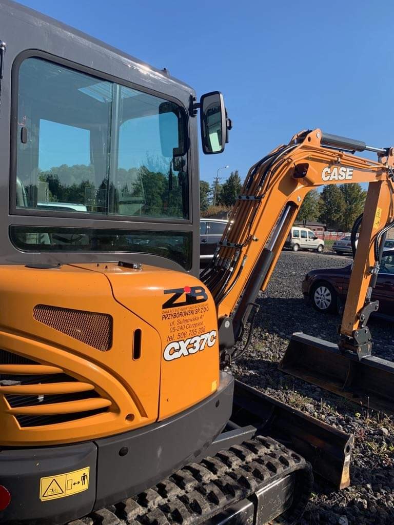 Pomarańczowa minikoparka Case CX37C z widocznym logo firmy ZB Przyborowski Sp. z o.o. na tle parkingu i zieleni.