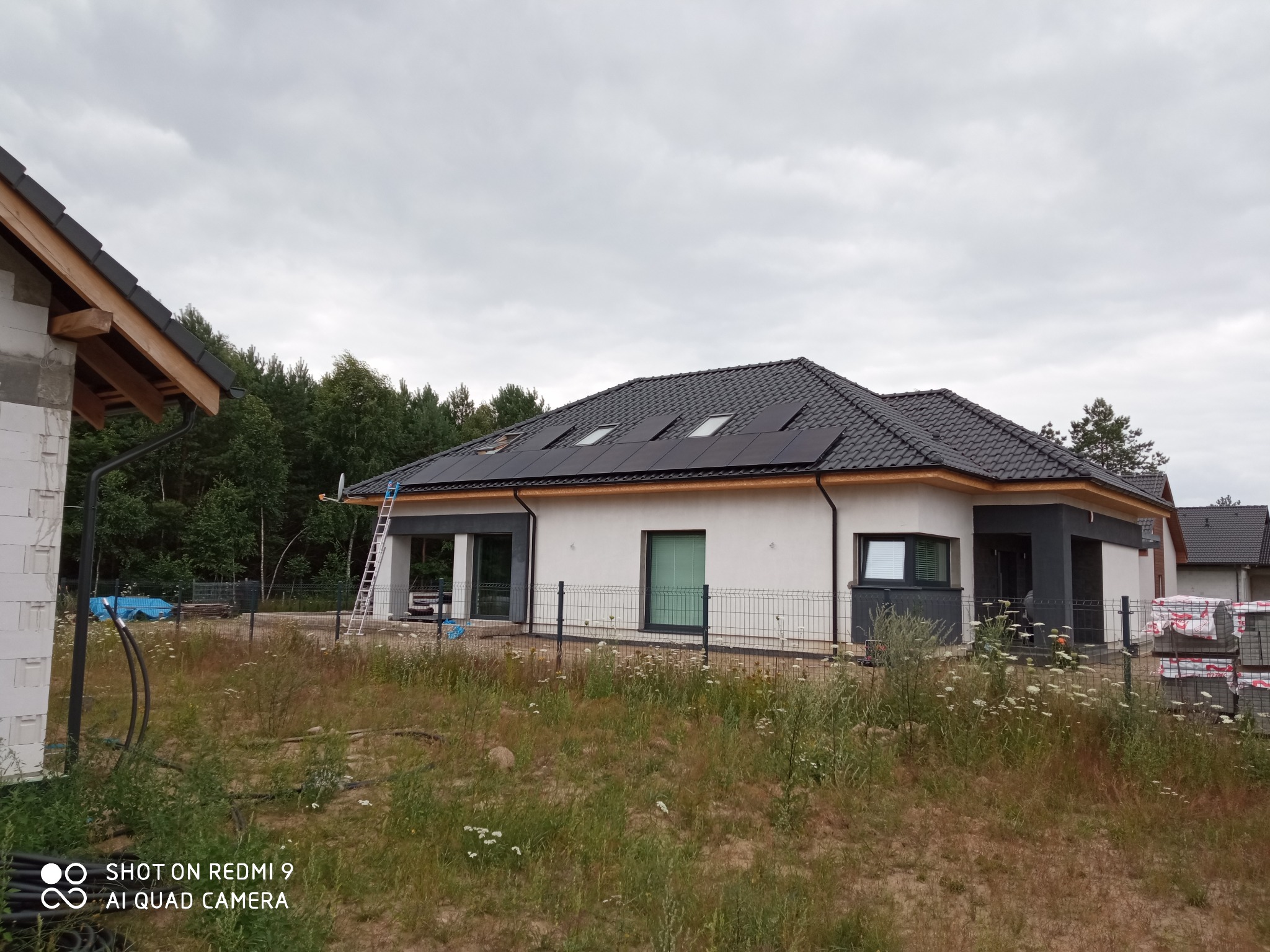 Dom jednorodzinny z panelami FullBlack na dachu, widoczna drabina oparta o dach oraz fragment budynku w trakcie budowy.