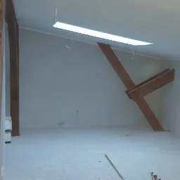 Poddasze po szpachlowaniu i malowaniu, widoczne drewniane elementy konstrukcyjne, białe ściany i sufit, oświetlenie LED w suficie, przygotowane do dalszych prac wykończeniowych.