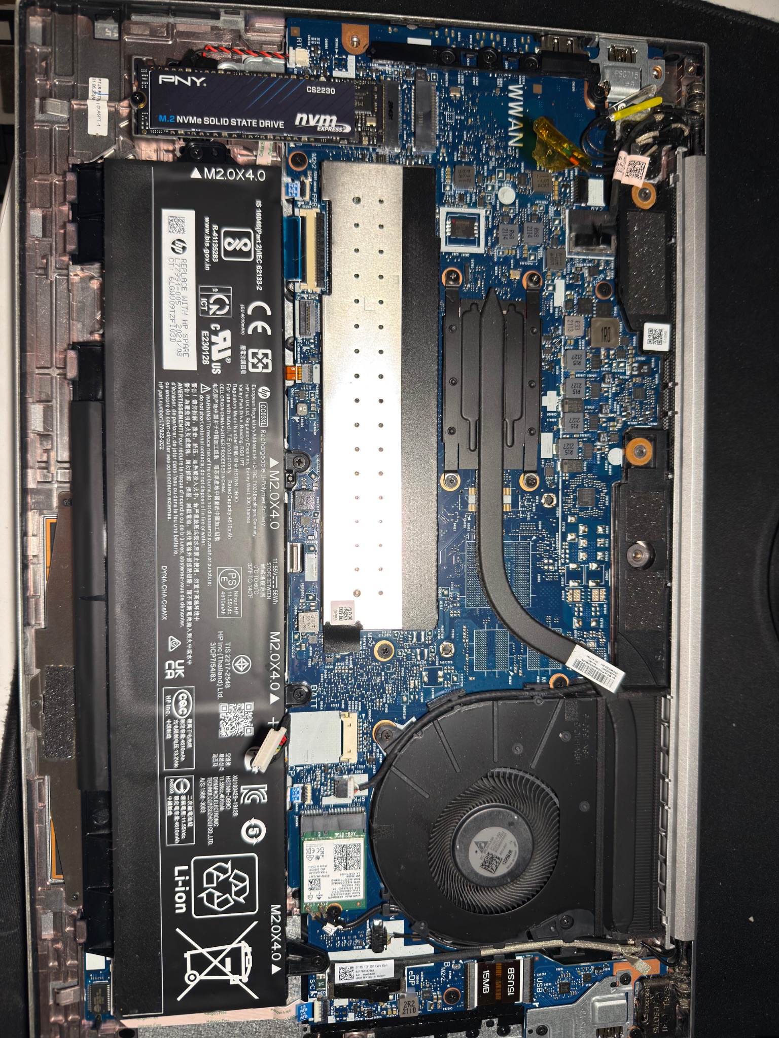 Wnętrze laptopa z widoczną baterią HP, dyskiem SSD PNY, wentylatorem i płytą główną. Detaliczne ujęcie elektroniki podczas naprawy lub modernizacji.