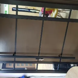 Nowoczesna brama garażowa segmentowa z przeszkleniami, brązowe panele z czarnymi akcentami, widoczne prowadnice i elementy montażowe, wnętrze garażu z wyposażeniem widoczne przez okna.