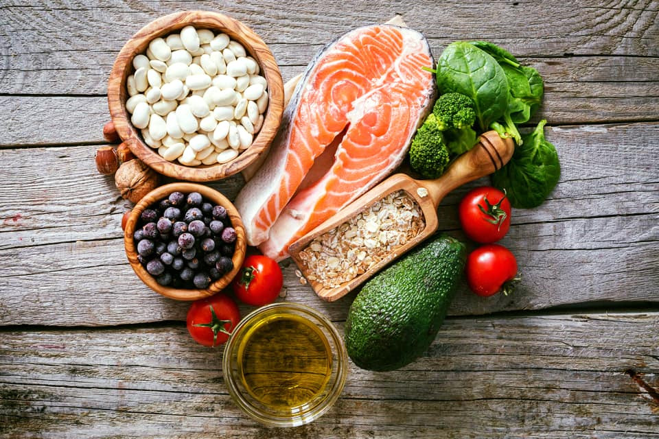 Kompozycja zdrowej żywności na drewnianym stole: łosoś, biała fasola, jagody, płatki owsiane w drewnianej miarce, awokado, pomidory, brokuły, szpinak i oliwa z oliwek w szklanej miseczce.