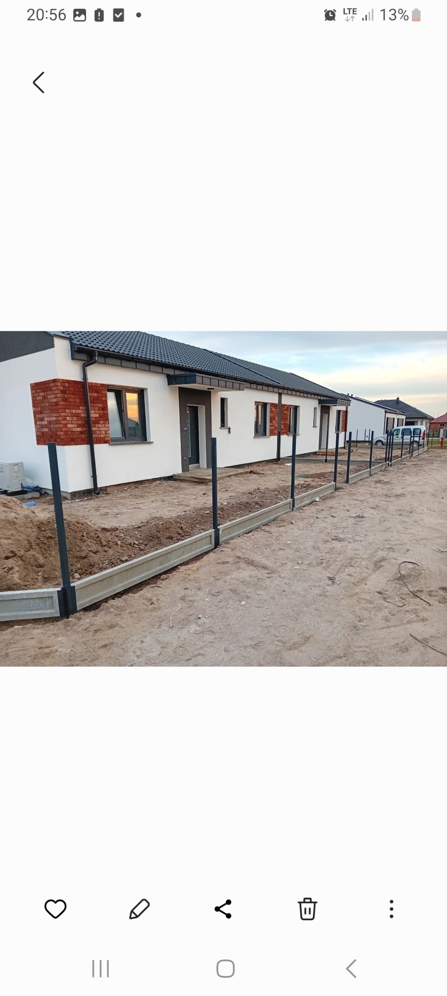 Wykop pod fundament ogrodzenia panelowego z zamontowanymi słupkami na tle szeregu domów jednorodzinnych.