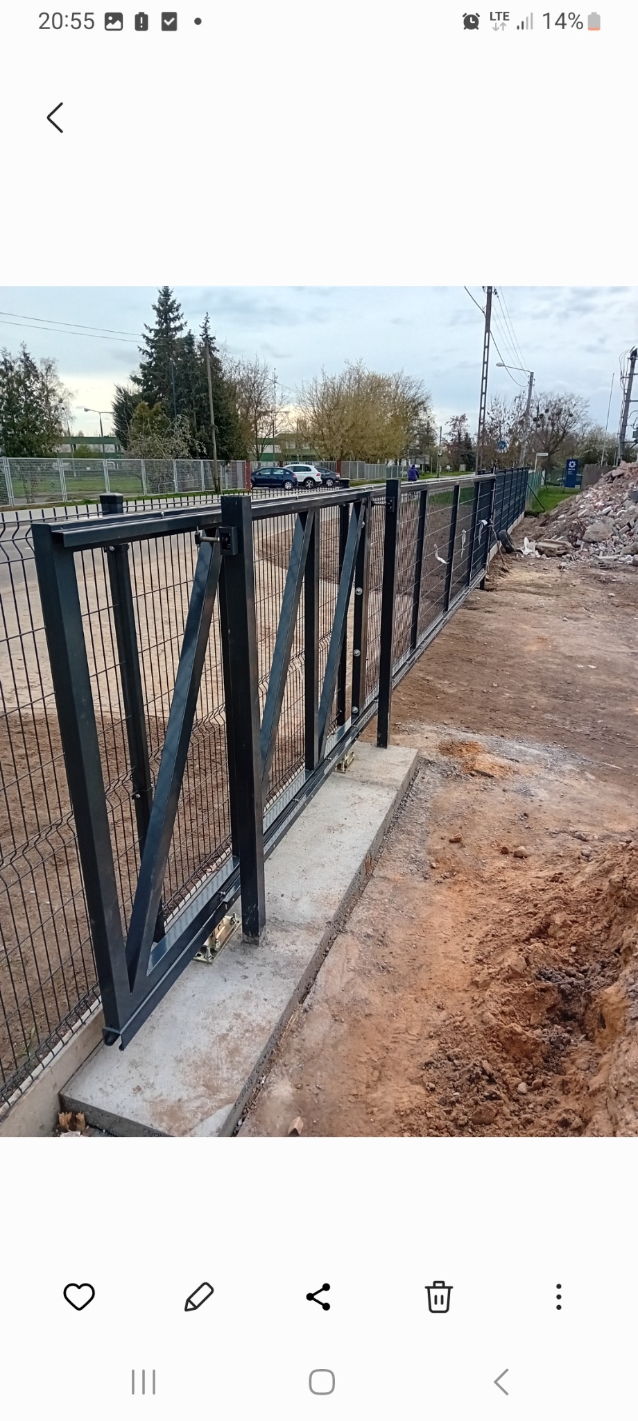 Montaż przesuwnej bramy panelowej z czarną ramą i widocznym mechanizmem jezdnym na betonowej podstawie, teren w trakcie prac ziemnych.