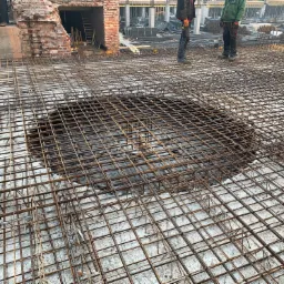 Zbrojenie płyty fundamentowej z widocznym otworem w Legnicy, przygotowane do zalania betonem, z fragmentem ceglanej konstrukcji w tle.