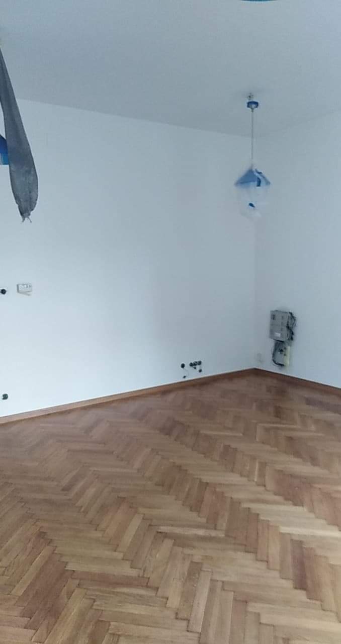 Nowo ułożony, jasny parkiet w jodełkę w pokoju z białymi ścianami i zabezpieczonymi elementami instalacji elektrycznej.