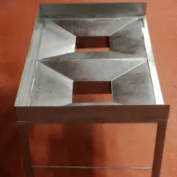 Stalowy stół gastronomiczny z otworami, spawany z profili kwadratowych, na tle pomarańczowej ściany.