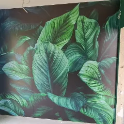 Pokój w trakcie wykańczania z ciemnozielonymi ścianami i fototapetą z motywem dużych, zielonych liści, widoczny surowy oścież drzwi.