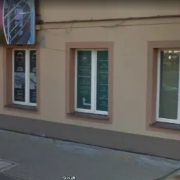 Fasada budynku z trzema oknami. W oknach widoczne plakaty informacyjne, w tym jeden z nazwą 'Kancelaria Adwokacka'. Nad drzwiami szyld z nazwą firmy i napisem 'Wejście'.