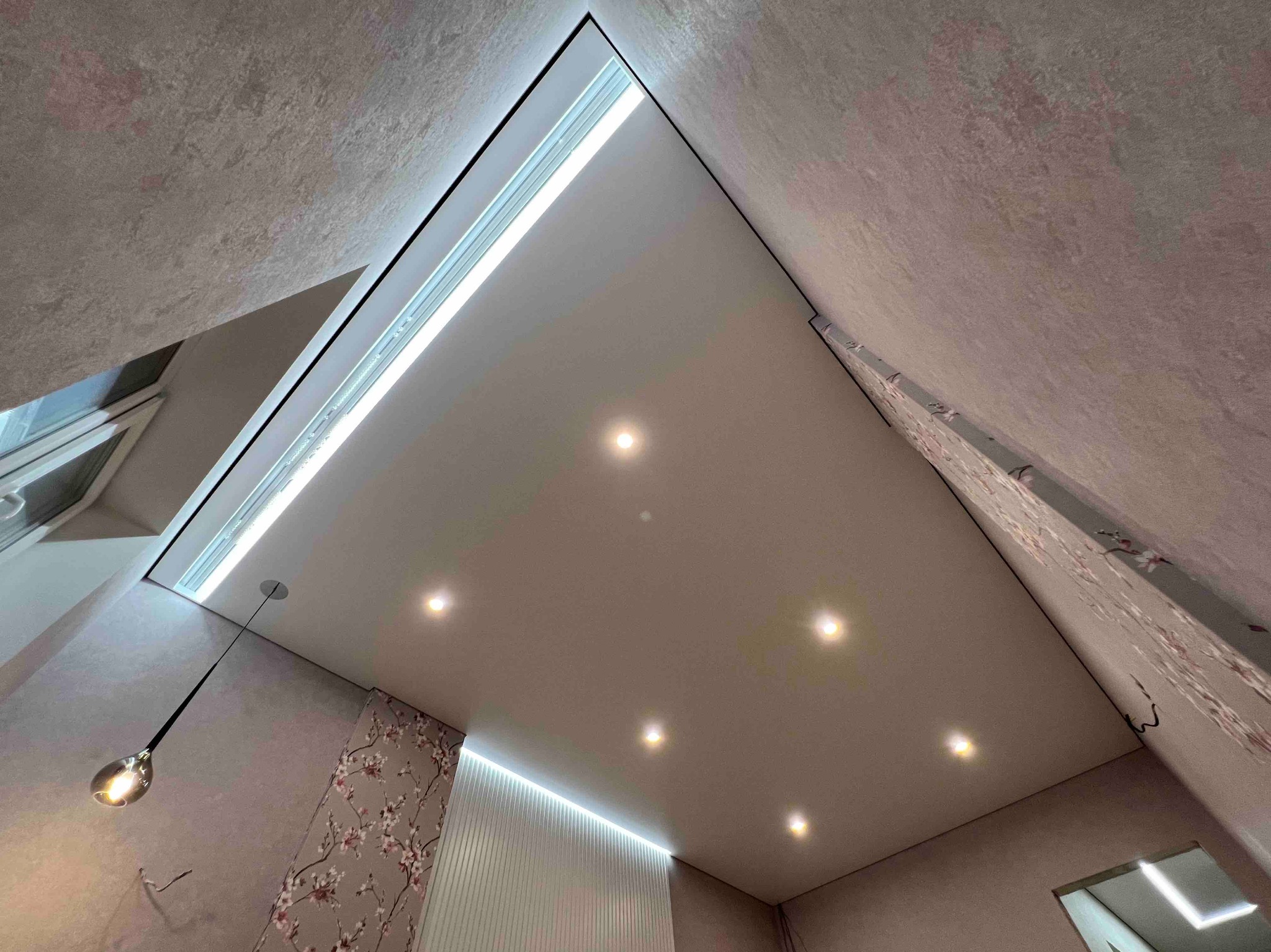 Sufit napinany z oświetleniem LED i wzorzystą tapetą, widok z dołu, z lampą wiszącą. Nietypowy kąt ujęcia podkreśla nowoczesny design.