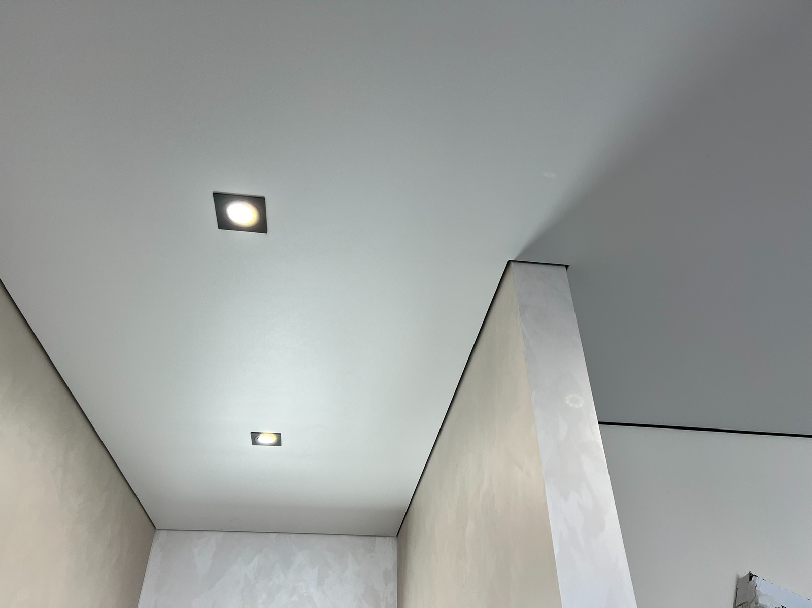 Biały sufit napinany z dwoma kwadratowymi lampami LED w nowocześnie wykończonym wnętrzu z dekoracyjnymi ścianami. Precyzyjne wykończenie, minimalistyczny design.