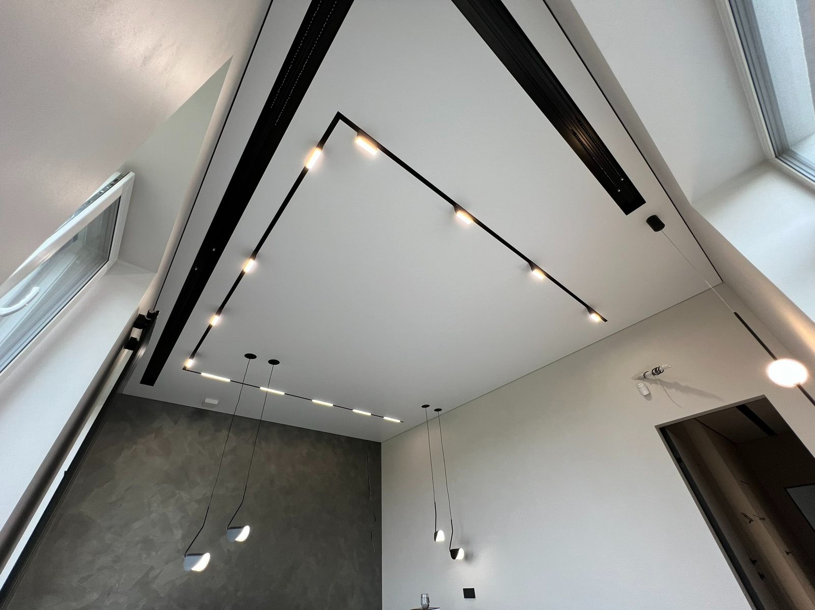 Biały sufit z czarnymi listwami LED, nowoczesne oświetlenie punktowe i wiszące lampy, szara ściana z efektem dekoracyjnym. Nowoczesne wykończenie wnętrza.