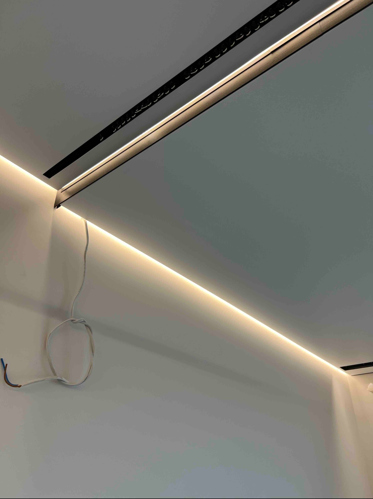 Nowoczesny sufit napinany z oświetleniem LED wzdłuż krawędzi, czarna listwa montażowa, przewody elektryczne widoczne w rogu. Minimalistyczny design.