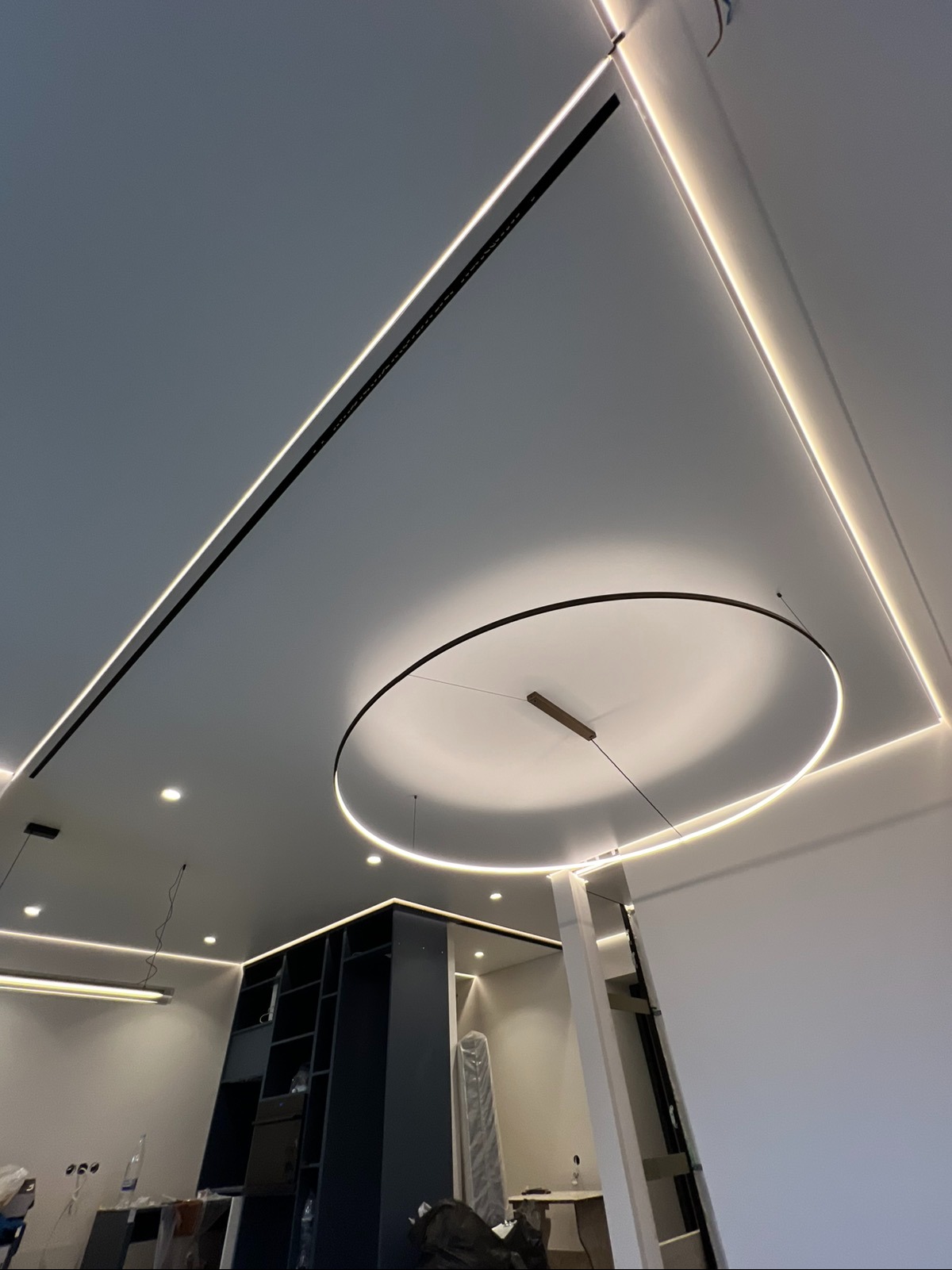 Nowoczesny sufit napinany z oświetleniem LED w kształcie okręgu i liniowymi listwami. Geometryczny design, minimalistyczne wnętrze, jasne światło.