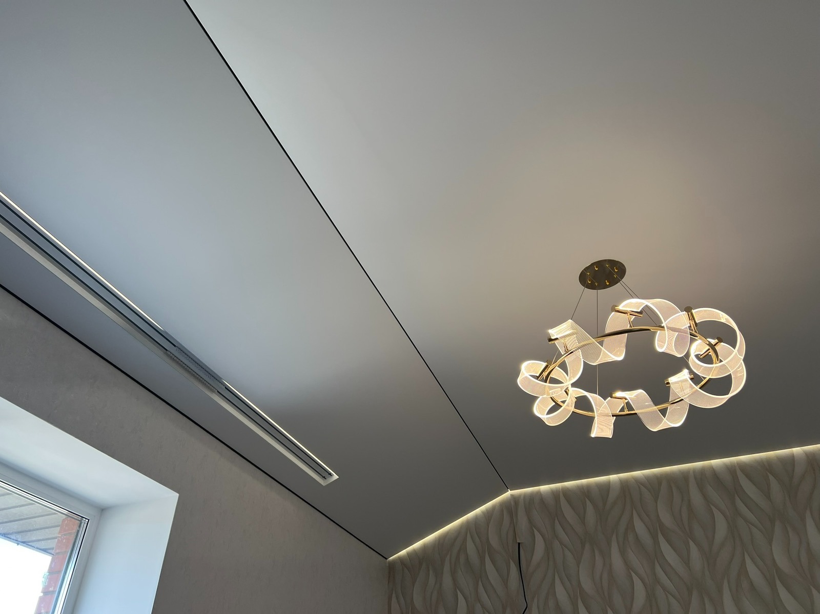 Biały sufit napinany z oświetleniem LED i designerskim, okrągłym żyrandolem. Nowoczesne wykończenie wnętrza, widok z dołu.