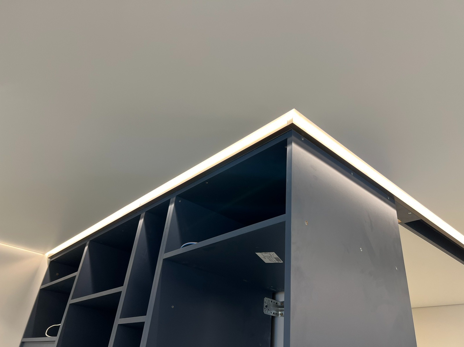 Niebieski regał z podświetleniem LED na suficie, widok z dołu, oświetlenie tworzy jasną linię, nowoczesny design, wykończenie wnętrz.