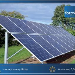 FotowolTech - Instalacja paneli słonecznych na trawiastym terenie, widoczne srebrne konstrukcje wsporcze, w tle drzewa i błękitne niebo z chmurami.