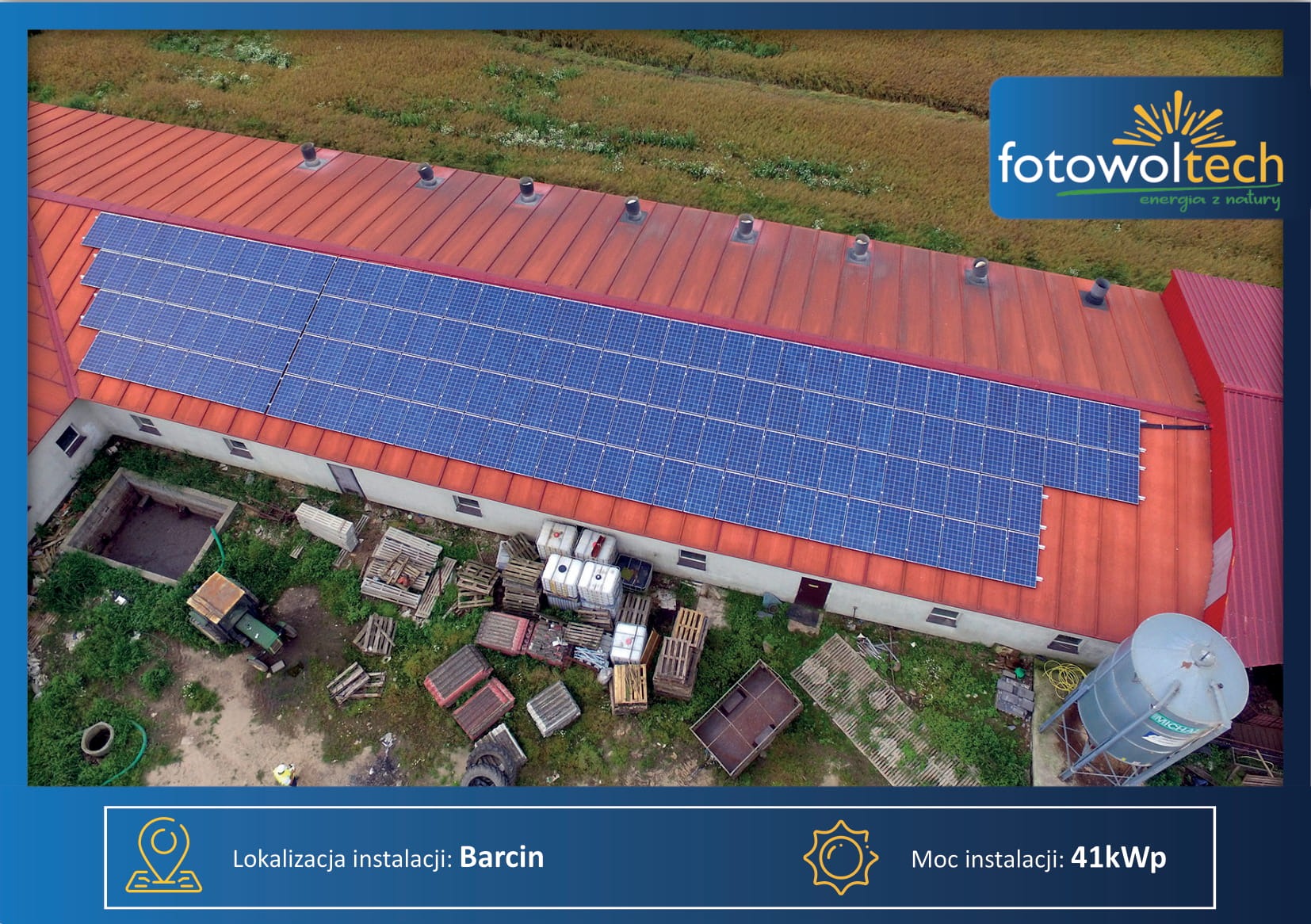 Widok z góry na instalację paneli słonecznych na czerwonym dachu budynku gospodarczego, z widocznym terenem wokół, traktorem, stertą palet i zbiornikiem. W tle pole uprawne i logo firmy.