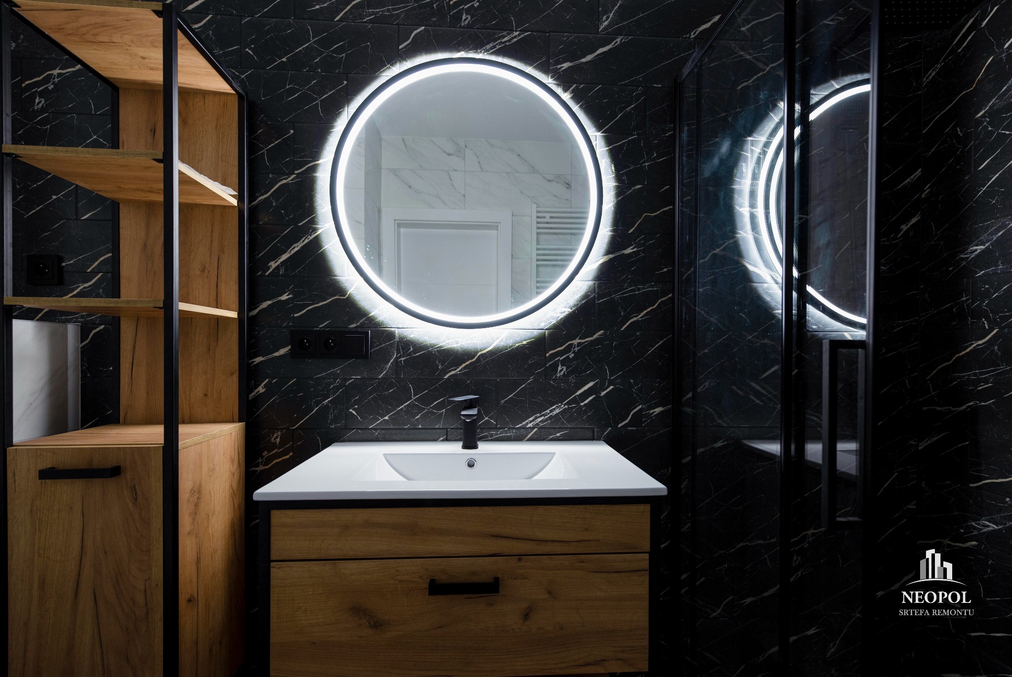 Nowoczesna łazienka z czarnymi marmurowymi płytkami, okrągłym lustrem z podświetleniem LED, drewnianą szafką pod umywalką i otwartym regałem z drewnianymi półkami.