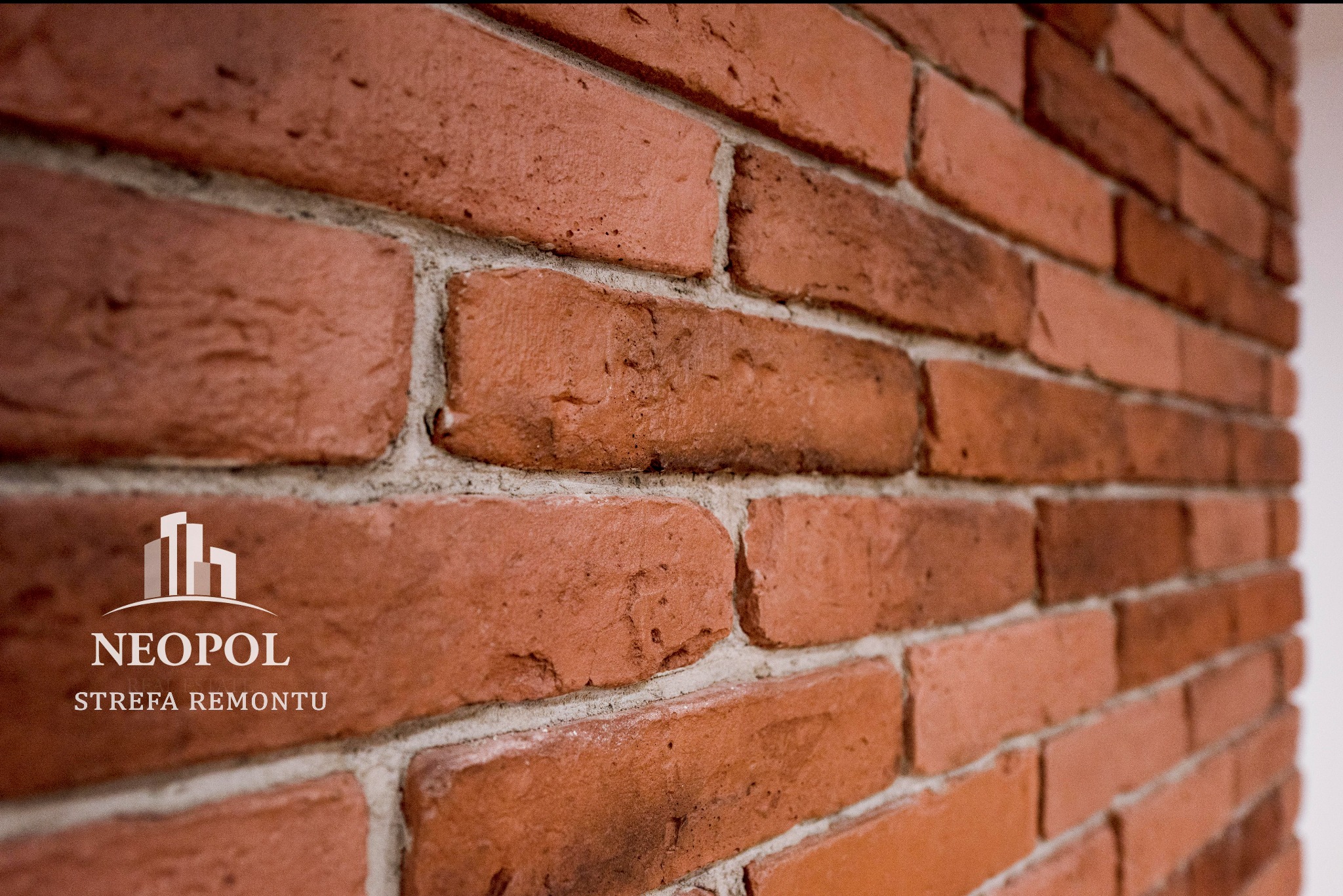 Ściana z cegły klinkierowej w odcieniach czerwieni, z widocznym logo firmy 'NEOPOL Strefa Remontu' na jednej z cegieł.