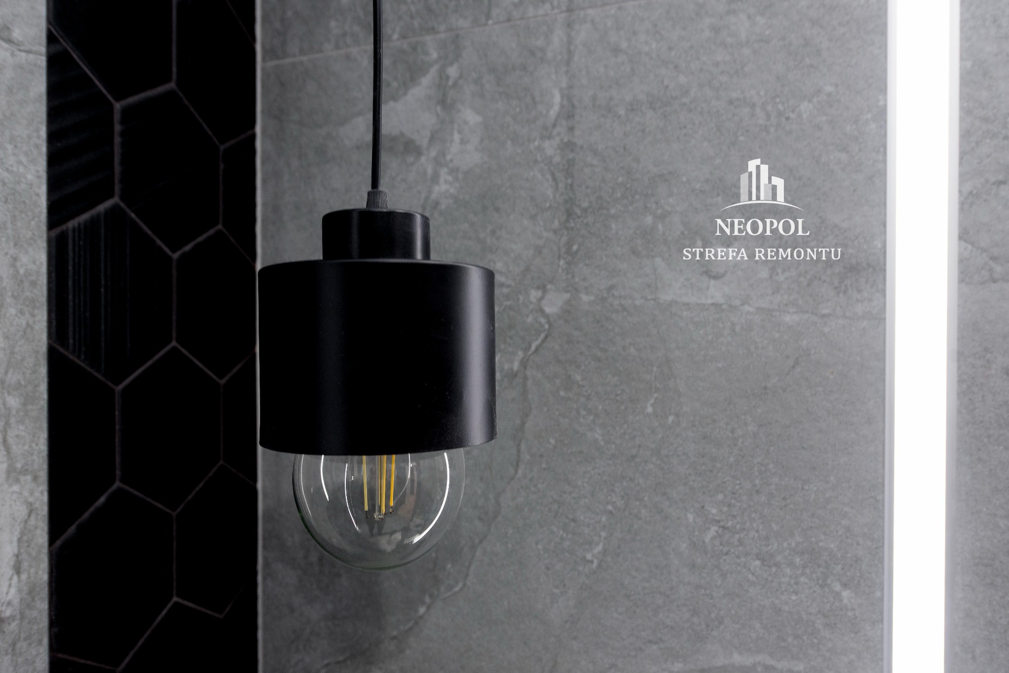 Czarna lampa wisząca z żarówką dekoracyjną na tle szarej ściany z logo 'NEOPOL Strefa Remontu' i fragmentem ściany z czarnych heksagonalnych płytek.
