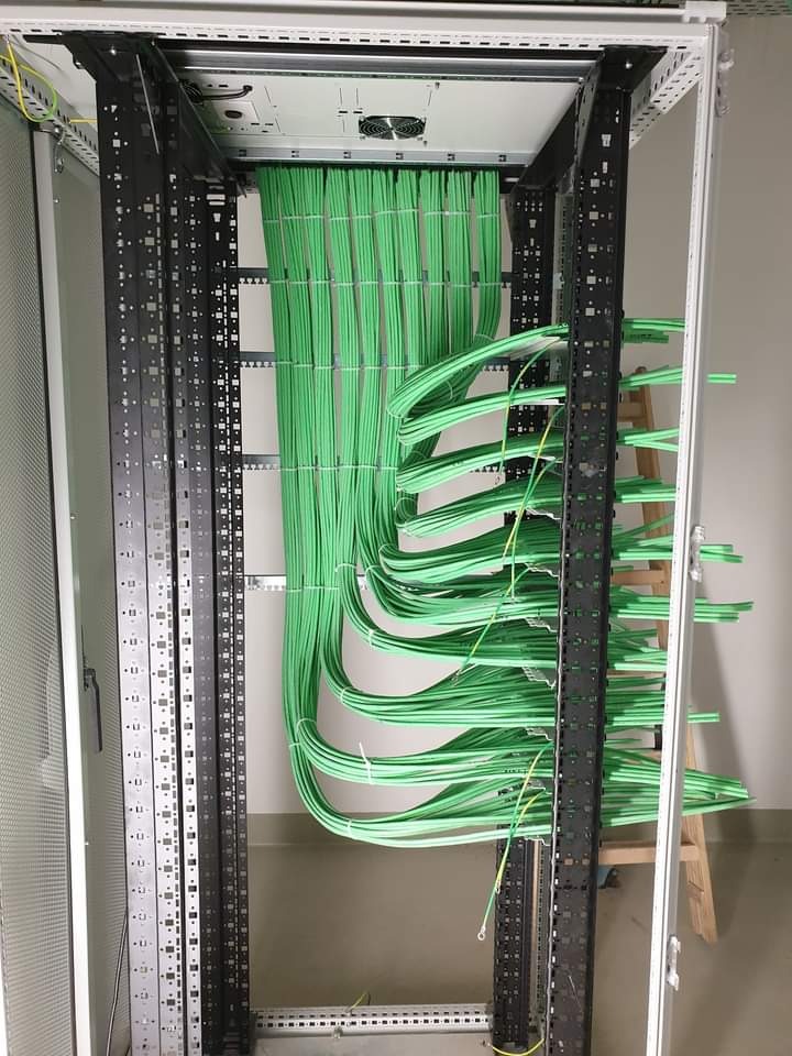 Widok z góry na szafę serwerową z uporządkowanymi, zielonymi kablami, ułożonymi w równych pętlach i przymocowanymi opaskami zaciskowymi.