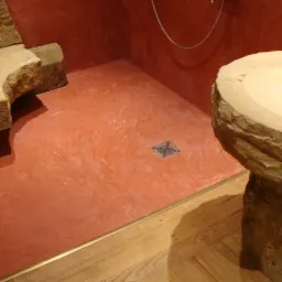 Wykończona łazienka z podłogą i ścianami w odcieniach terakoty, z kamienną umywalką na postumencie i elementami dekoracyjnymi z piaskowca