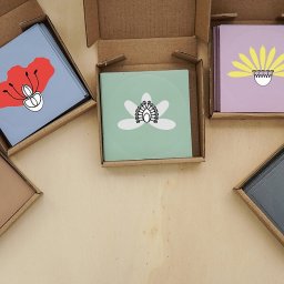 Julia Gabryszewska - Zestaw kwadratowych kartoników z minimalistycznymi ilustracjami kwiatów w otwartych, tekturowych pudełkach na drewnianym tle.