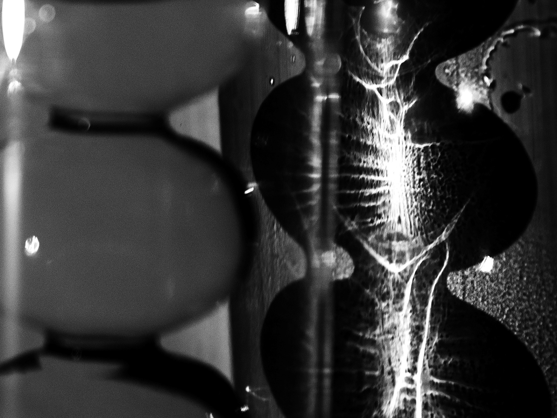 Czarno-białe ujęcie abstrakcyjnej kompozycji z elementami przypominającymi piasek w klepsydrze i rozmyte kształty kuliste, oświetlone w sposób tworzący kontrastowe refleksy.