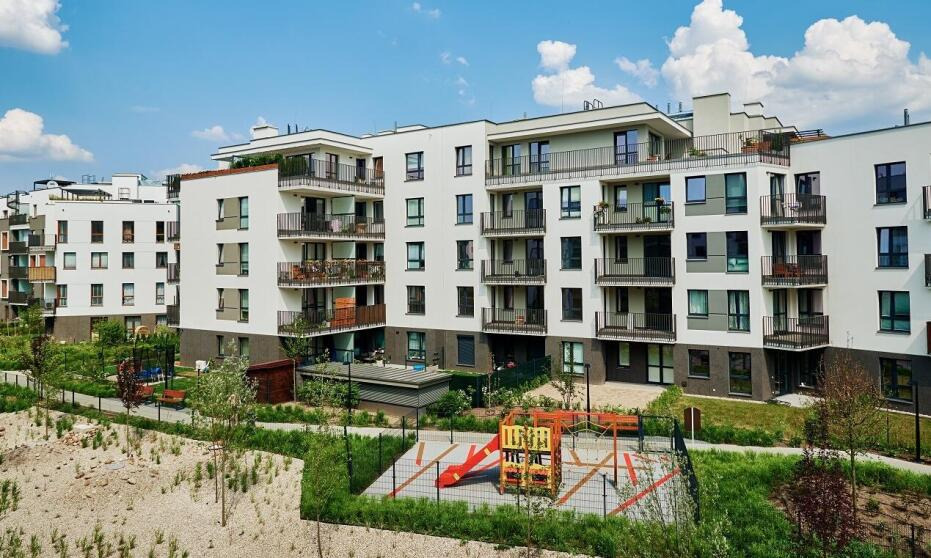 Nowoczesne, białe budynki apartamentowe z balkonami i placem zabaw w Warszawie, widok z góry w słoneczny dzień.