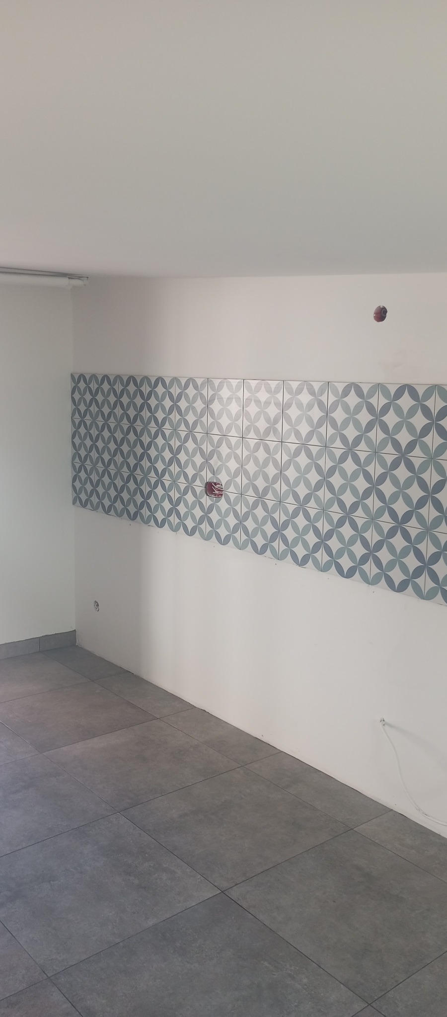 Świeżo położone, szare płytki podłogowe i dekoracyjne płytki ścienne z motywem w Borzechowie. Widoczne gniazdka elektryczne i fragment listwy oświetleniowej.