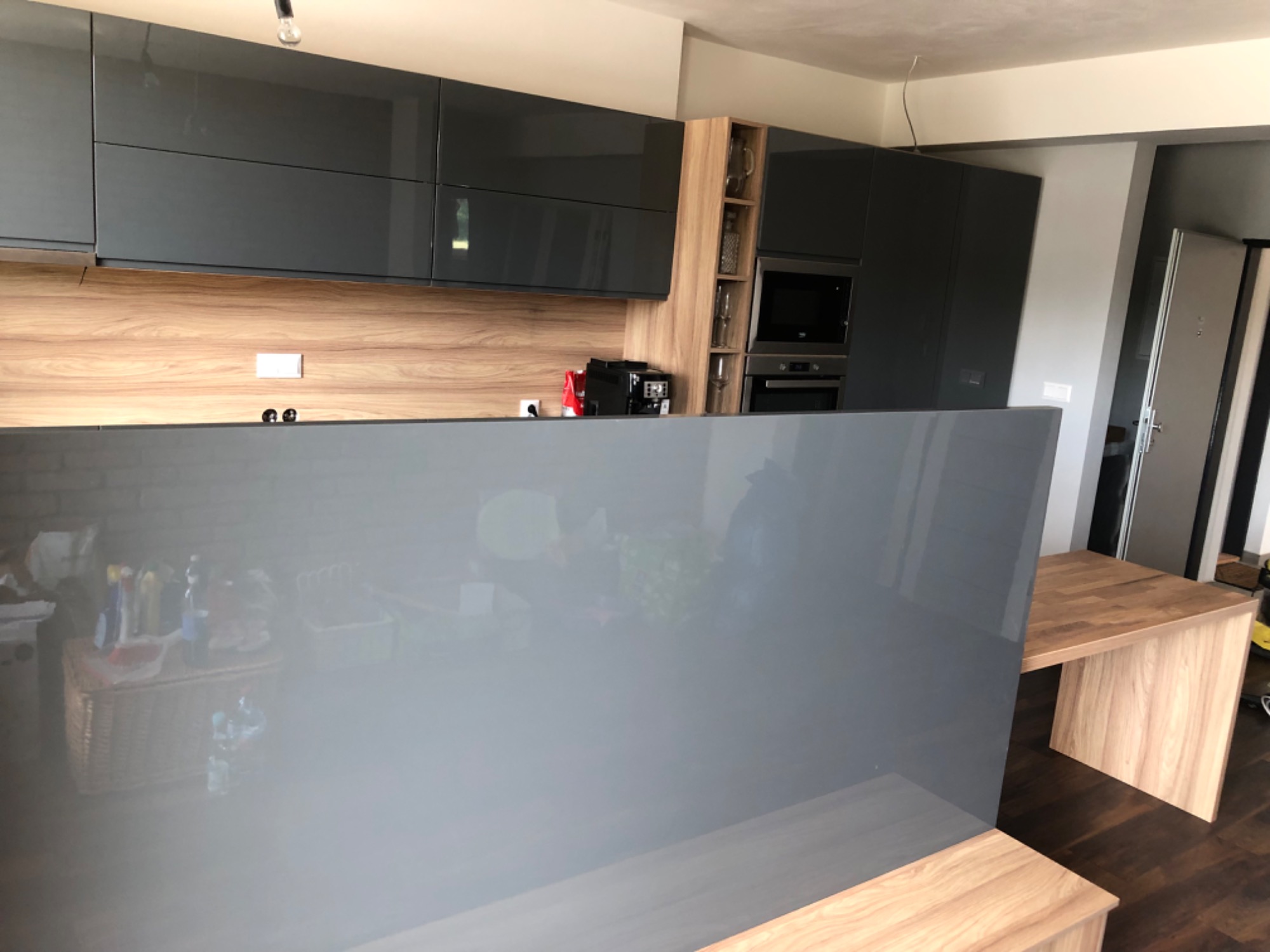 Nowoczesna kuchnia z szarymi szafkami i drewnianym blatem, widok zza półwyspu kuchennego, ekspres do kawy i piekarnik w zabudowie.