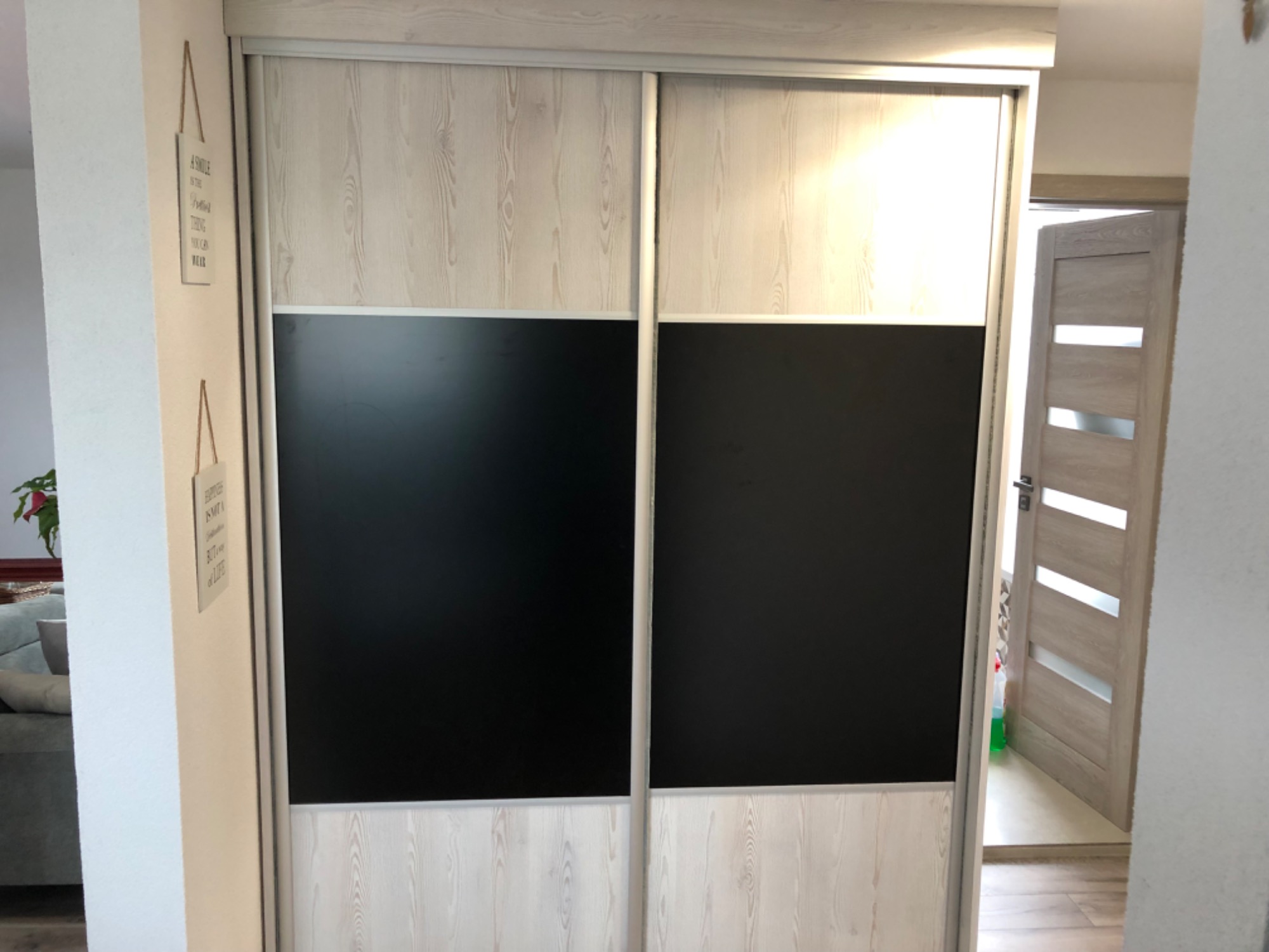 Dwudrzwiowa szafa przesuwna z czarnymi panelami i jasnym drewnem, widziana z bliska w mieszkaniu w Krakowie, z widocznym fragmentem drzwi wejściowych w tle.