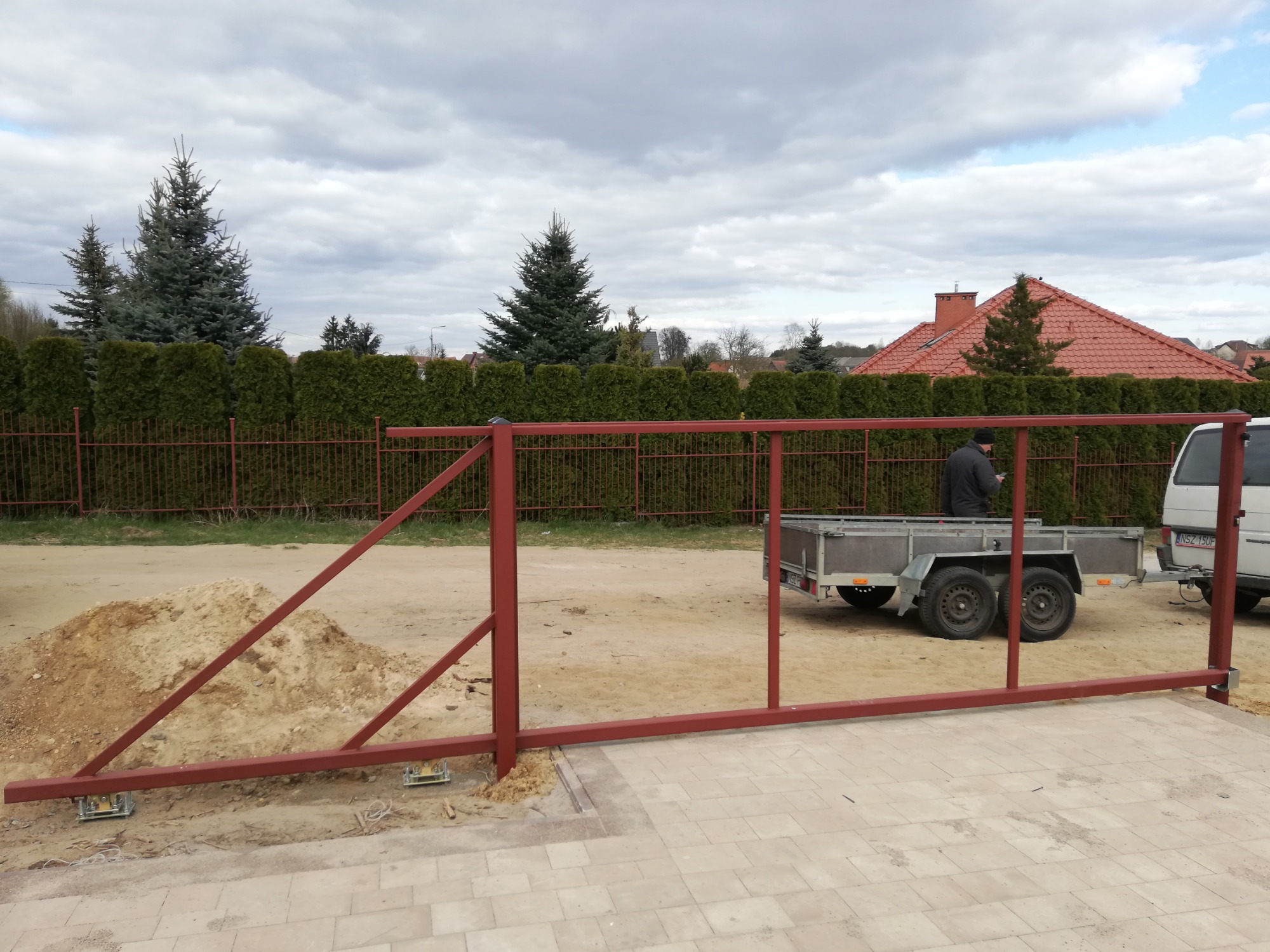 Montaż bramy przesuwnej z profili stalowych na posesji, widoczny fragment ogrodzenia, przyczepa i samochód dostawczy w tle.