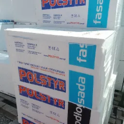 Pakiety białego materiału izolacyjnego z nadrukowanym logo producenta Polstyr, przeznaczone do ocieplenia fasad i podłóg, ułożone jeden na drugim.