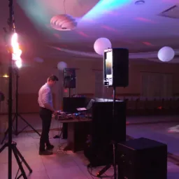 DJ w trakcie pracy z oświetleniem scenicznym i nagłośnieniem na sali bankietowej z dekoracjami.
