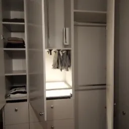 Wnętrze szafy z szufladami i półkami, oświetleniem LED i drążkiem na ubrania, widoczne ubrania na wieszakach.