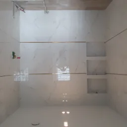 Wykończona łazienka z białymi płytkami imitującymi marmur, złotymi listwami dekoracyjnymi i wnękami w ścianie, widok z dołu na sufit z oświetleniem punktowym.