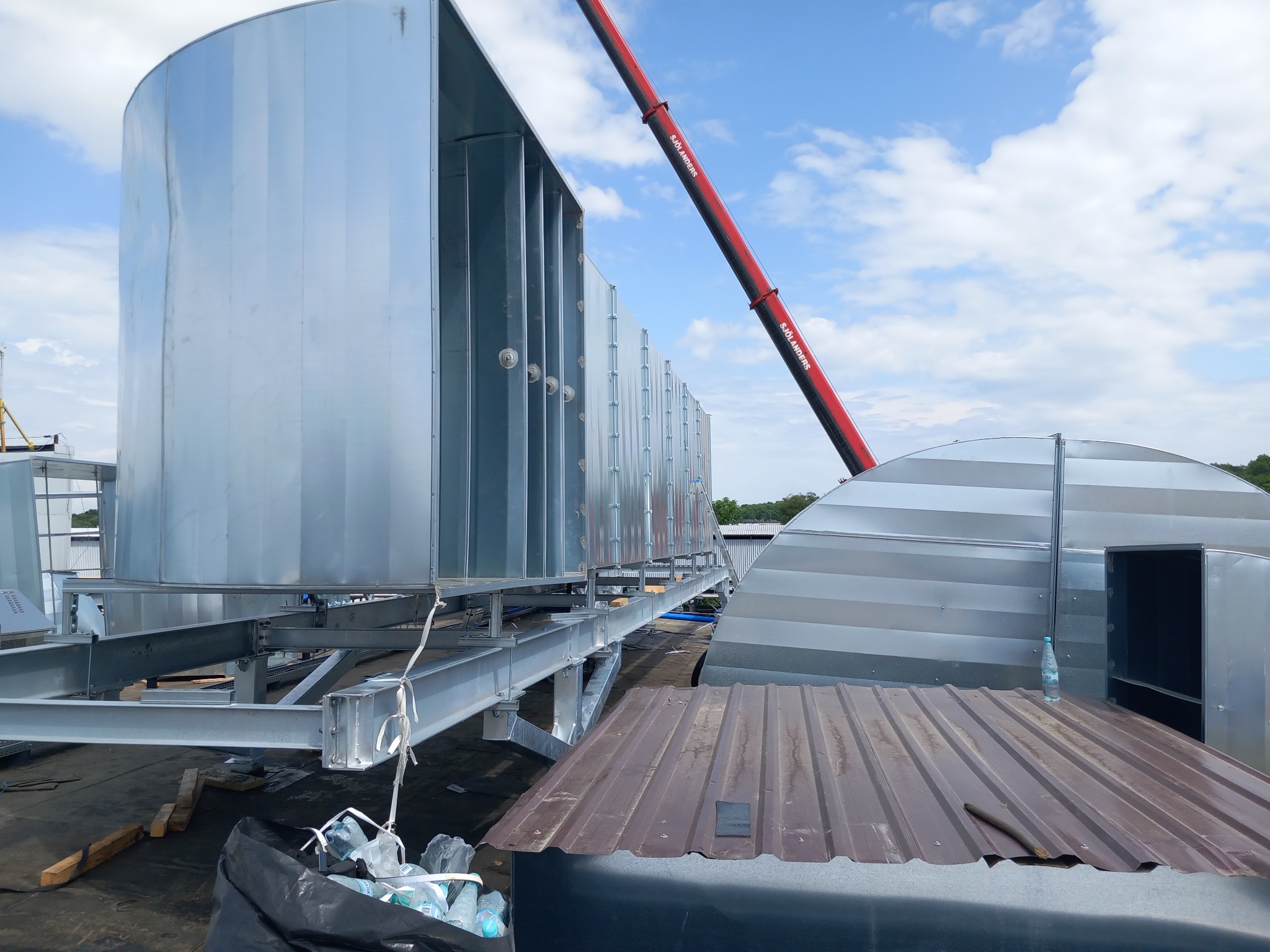 Montaż przemysłowej instalacji wentylacyjnej na dachu budynku, widoczne elementy konstrukcyjne i dźwig z logiem Sjolanders.