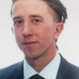 Portret mężczyzny w ciemnym garniturze i krawacie, z zaczesanymi do tyłu włosami, na jasnym tle.