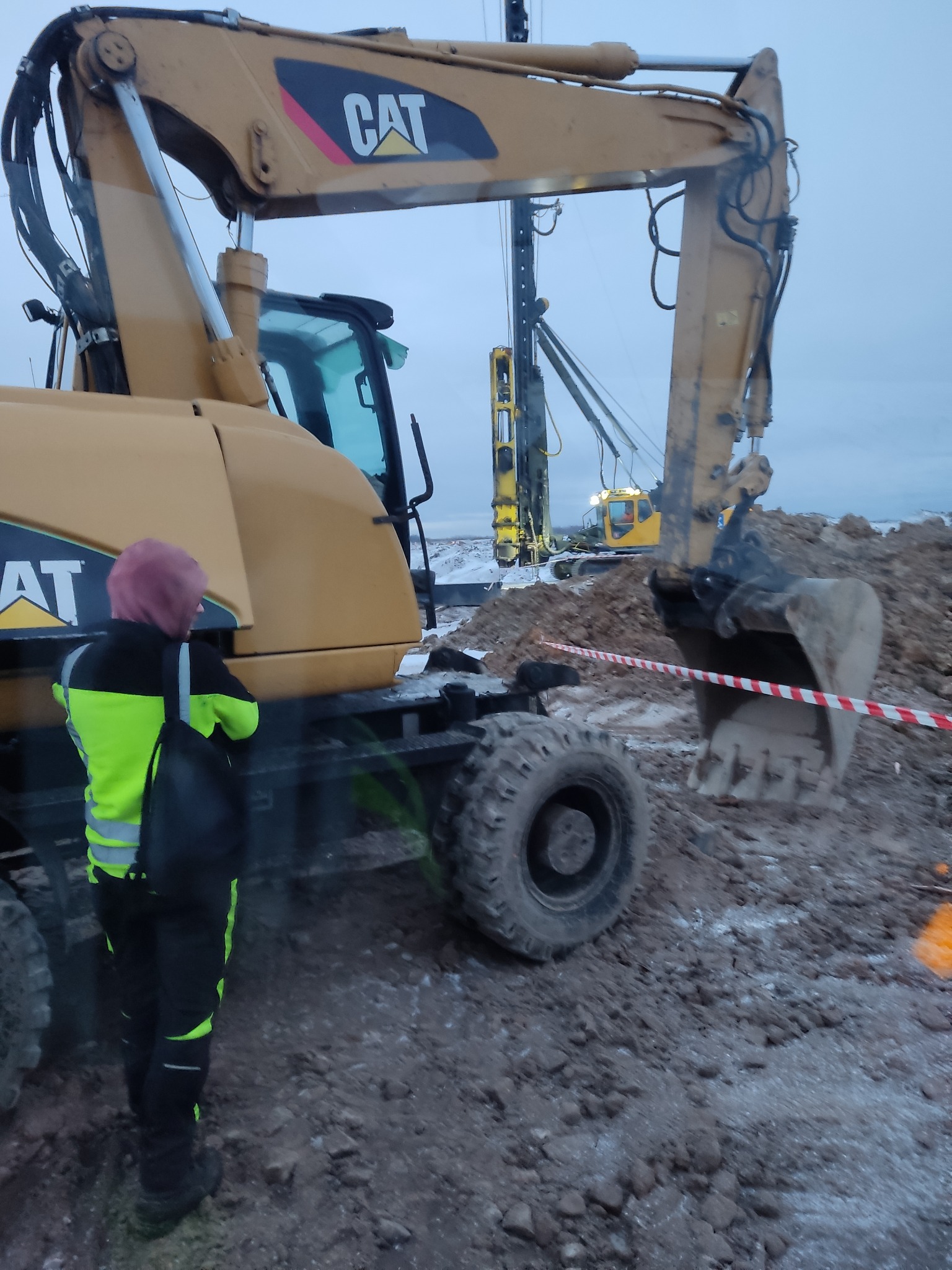 Żółta koparka CAT w Damnicy na placu budowy, z pracownikiem w odblaskowej kamizelce i wykopaną ziemią w tle.