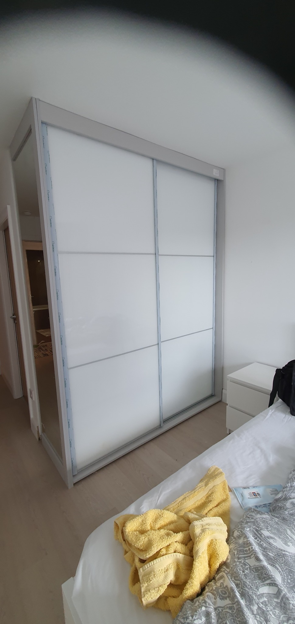 Biała szafa wnękowa z przesuwnymi drzwiami w sypialni w Dublinie, widok na częściowo otwarte drzwi do innego pomieszczenia.