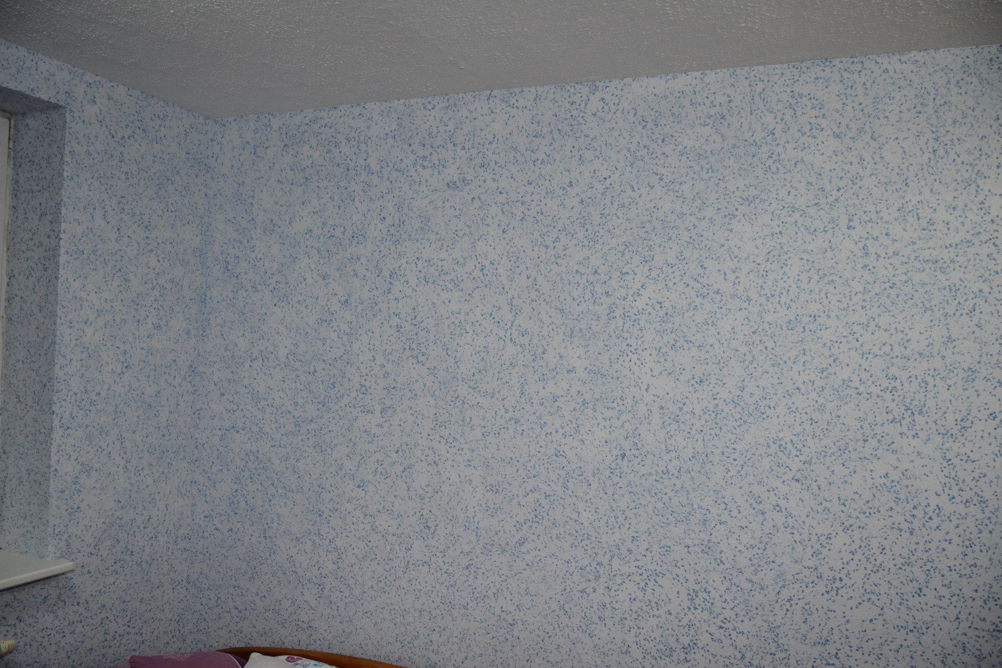 Ściana pokryta tynkiem strukturalnym w odcieniach błękitu i bieli, widok z dołu ukazujący narożnik z oknem i fragment sufitu.